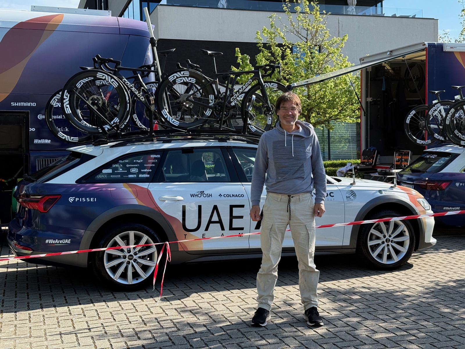 The fan behind Tadej Today standing beside the UAE Team Emirates team car, race bikes loaded on the roof